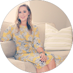 Natlie smiling while seated on a couch, wearing a floral dress