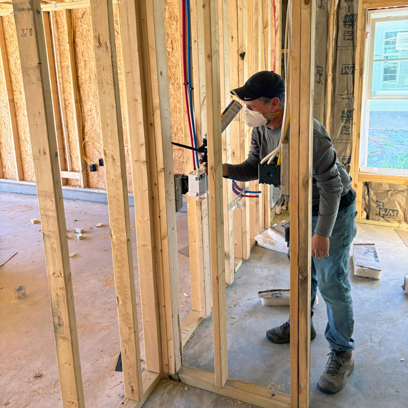Person installing air-sealing in framed building interior, wearing protective mask