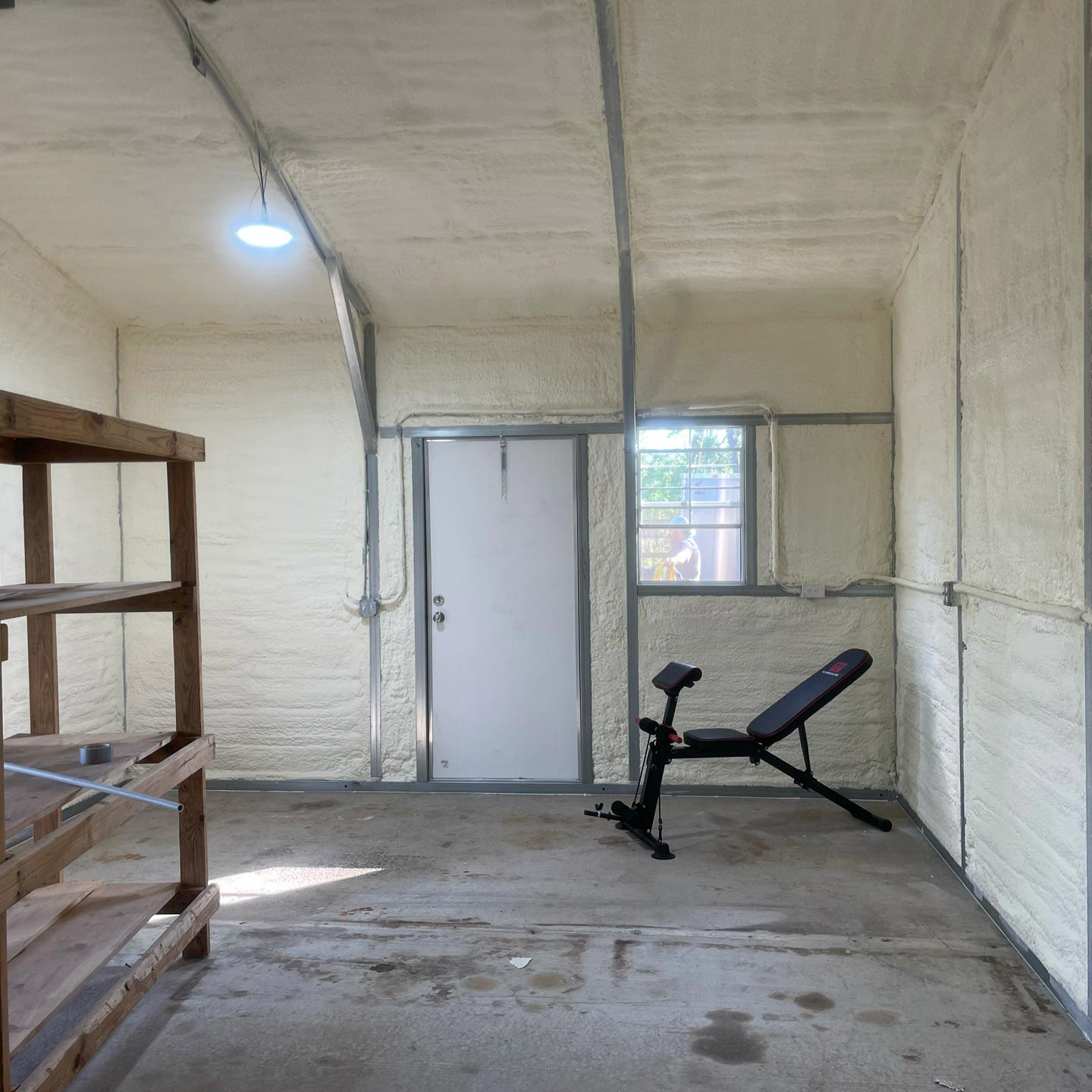 Finished garage with spray foam insulation, exercise bench, wooden shelves, and a lit ceiling