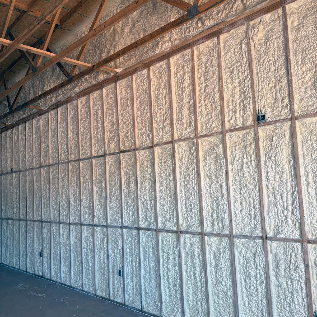 Spray foam insulation applied in a commercial building, covering walls and ceiling with wooden framing