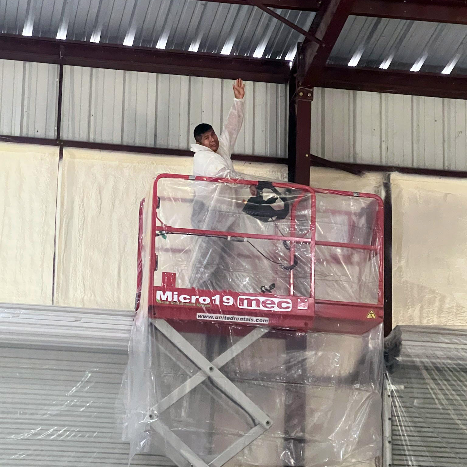 Person in protective gear on lift spraying foam in commercial space