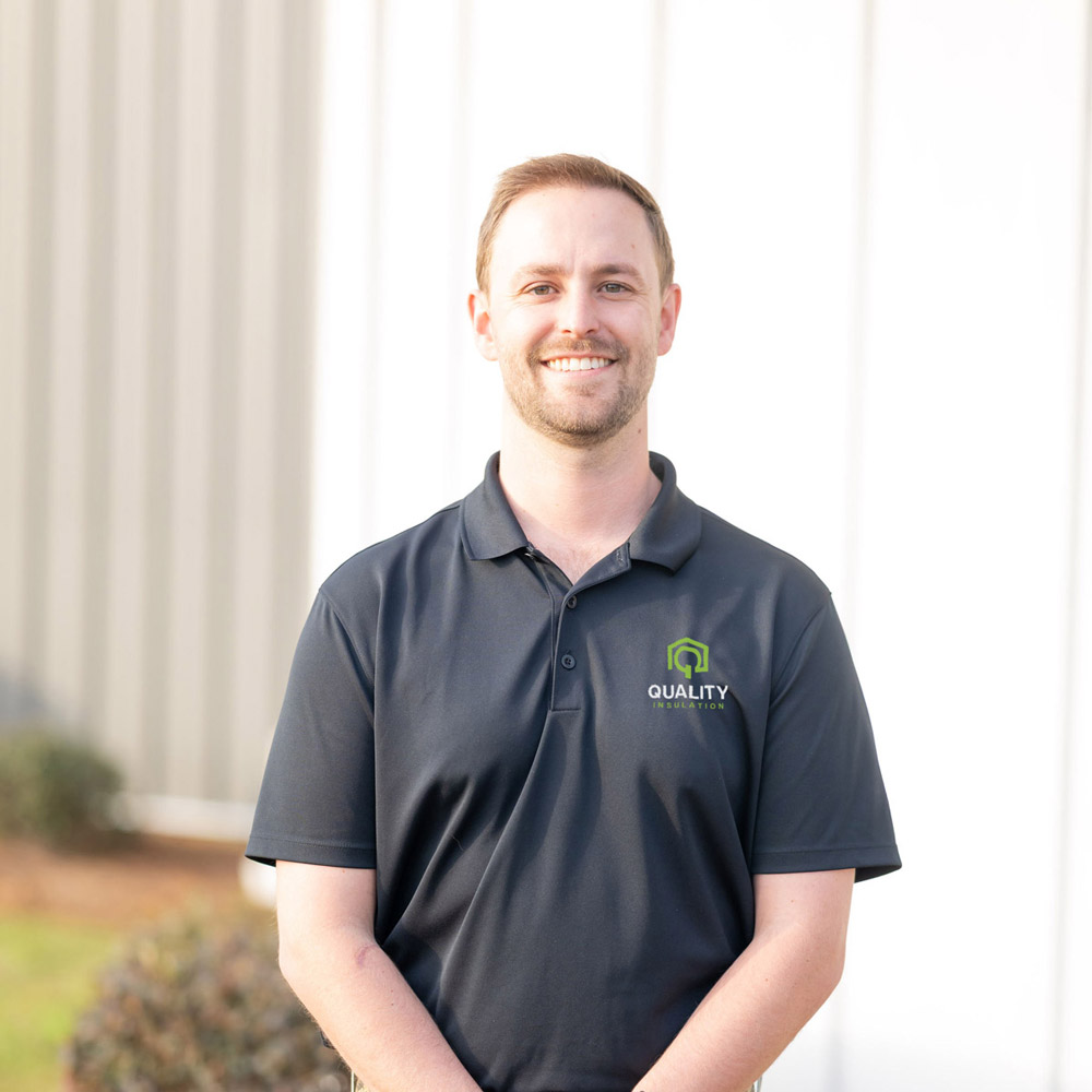 Smiling man in a black polo shirt with "Quality Insulation" logo stands outdoors