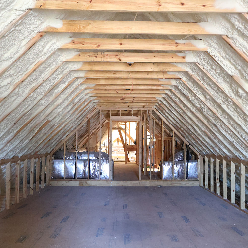 Unfinished attic with exposed wooden beams and spray foam insulation along the ceiling