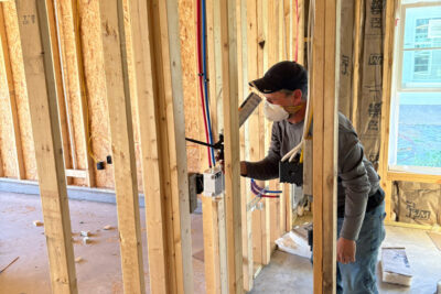 Technician air sealing electrical penetrations inside the wall framing of a new home before insulation installation.