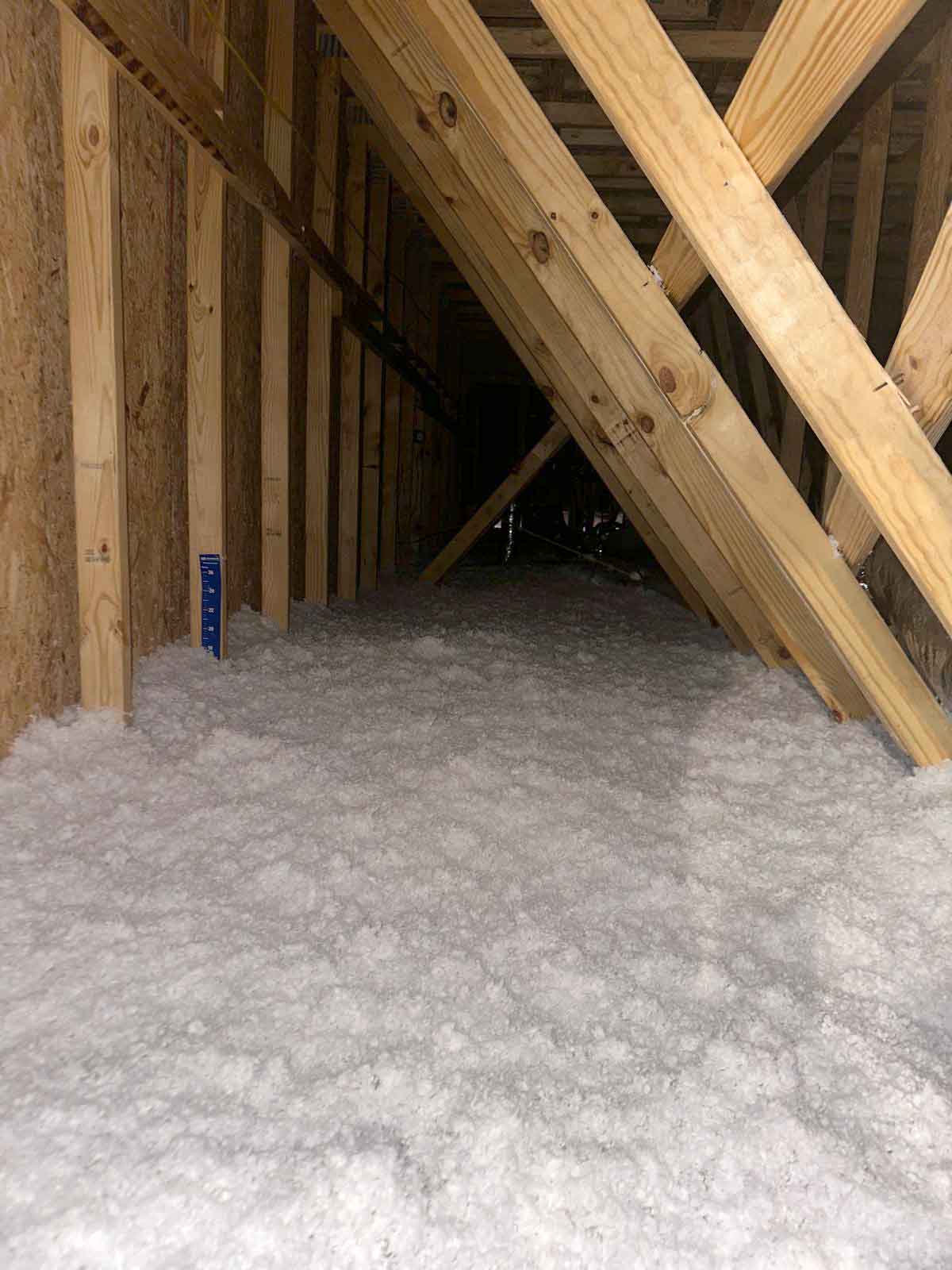 Quality Insulation of Valdosta blew loose-fill fiberglass insulation across an apartment attic floor, with a depth ruler marking the installed level, in Valdosta, GA.