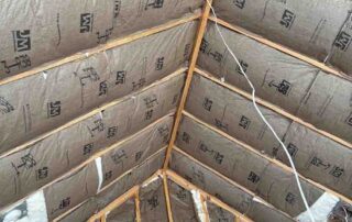 Quality Insulation of Valdosta installed kraft-faced R-38 fiberglass batts between vaulted roof rafters up to the ridge, with batts in the gable wall around two HVAC supply boots, in a new home.